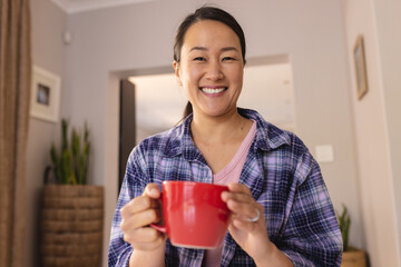 Portrait of happy asian woman holding mug, looking at camera and smiling