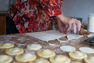 Unrecognizable aged woman cutting puff pastry with a glass to prepare dumplings