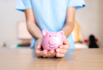 Hand gently and carefully holding a smiling piggy bank. Concept of taking good care of your money and making it work