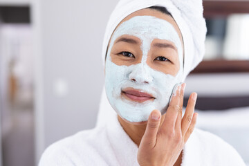 Portrait of happy asian woman applying beauty face mask in bathroom
