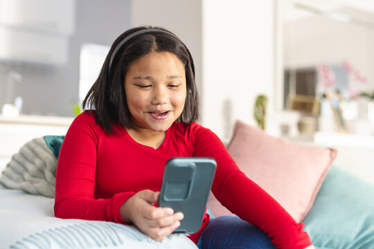 Happy asian girl sitting on sofa in living room and using smartphone