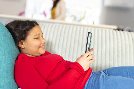Happy asian girl sitting on sofa in living room and using smartphone