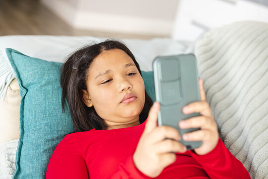 Happy asian girl sitting on sofa in living room and using smartphone