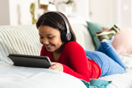 Happy asian girl sitting on sofa in living room and using tablet