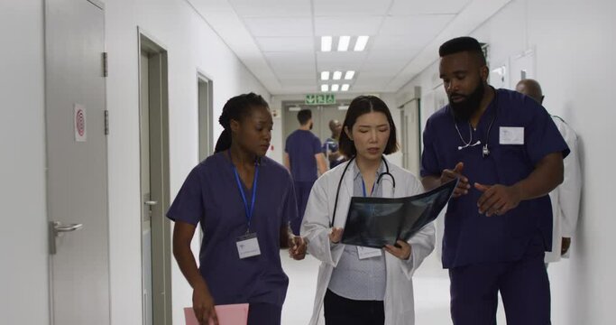 Video of three diverse male and female doctors walking in hospital corridor discussing x-ray