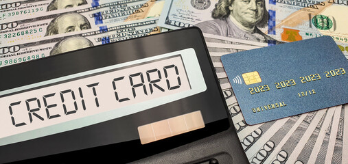 A calculator with the words "credit card" on the screen against the background of 100 US dollars banknotes. The concept of getting money on credit