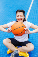 Smiling sportswoman with basketball on background of blue sports court. Sport and hobby concept.