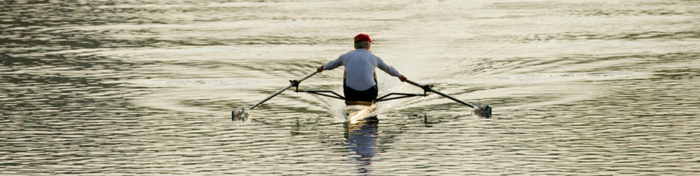 A lone rowing scull cuts through the river's glassy surface as the rower gets some early morning exercise.