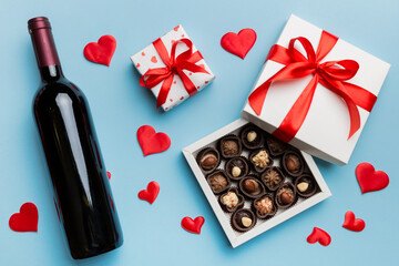 Bottle of red wine on colored background for Valentine Day with gift and chocolate. Heart shaped with gift box of chocolates top view with copy space