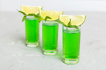 Sweet refreshing mint liqueur, with ice and mint leaves on table background, Shots with lime slice and mint flat lay