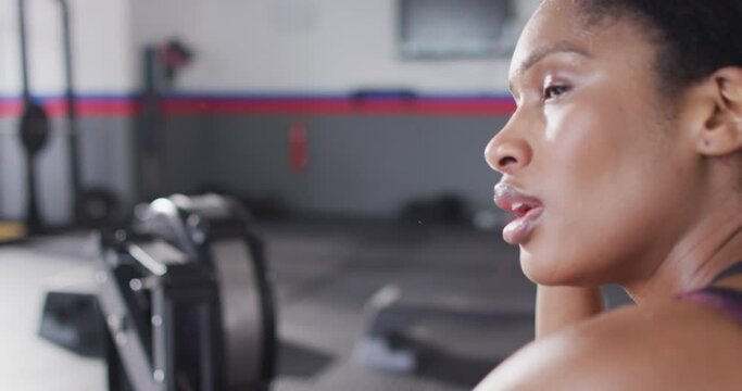 Video of tired african american woman on rowing machine recovering after working out at a gym