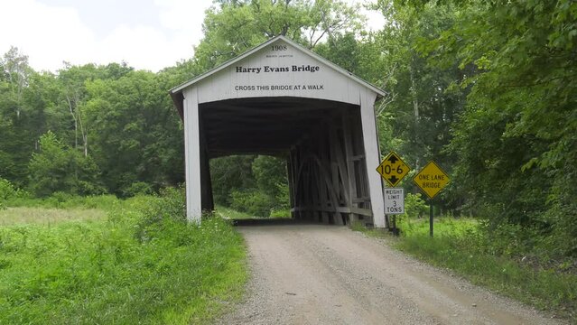 Harry Evans Covered Bridge near Rosedale IN. Shot starts as medium wide of a bridge portal that shows it leaning to the left, then zooms in. Bridge is on a county road and see routine vehicle traffic.