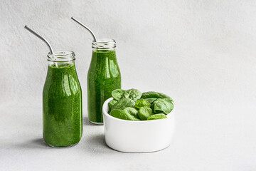 Green spinach smoothie in small glass bottles and spinach leaves in bowl.