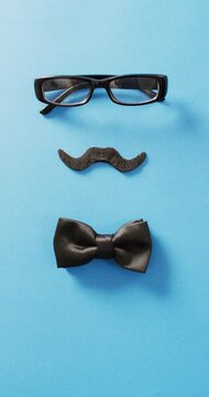 Vertical video of black false moustache, glasses and bow tie on blue background with copy space