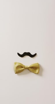 Vertical video of black false moustache and yellow bow tie on white background with copy space