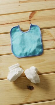 Vertical video of close up of white booties and blue bib on wooden background with copy space