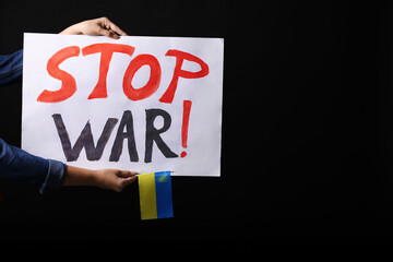 Woman holding Ukrainian flag and poster with words Stop War on black background, closeup