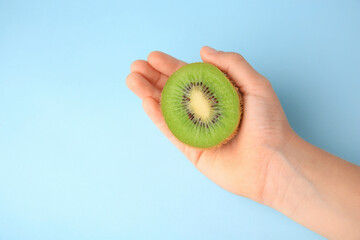 Woman holding cut fresh kiwi on light blue background, top view. Space for text