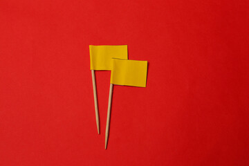Small yellow paper flags on red background, flat lay - obrazy, fototapety, plakaty