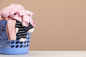 Plastic laundry basket with clothes near beige wall. Space for text