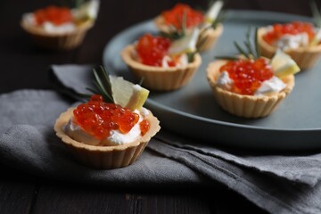 Delicious tartlets with red caviar and cream cheese served on wooden table, closeup