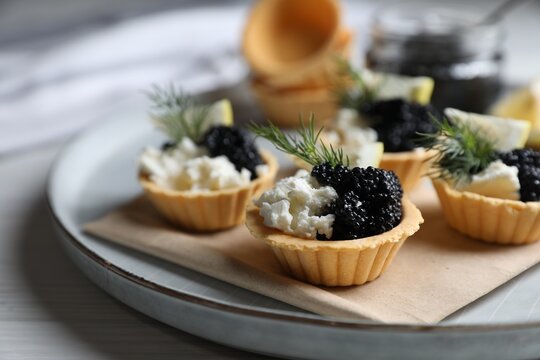 Delicious tartlets with black caviar, cream cheese and lemon served on light table, closeup