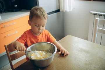 the child cooks in the kitchen, stirring the dough in a metal bowl