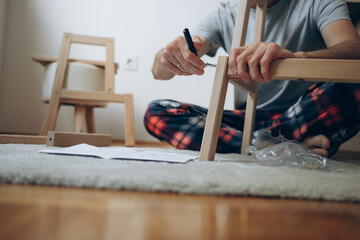 a man collects wooden furniture with his own hands while sitting on the floor in an apartment