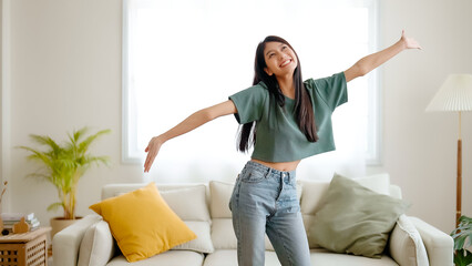 Young asian woman dancing on the floor in living room at home. Happy asia female smile relaxing in...