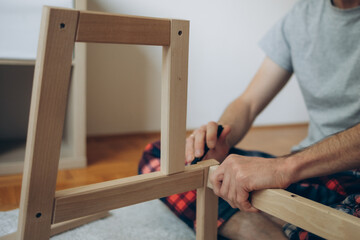 a man collects wooden furniture with his own hands while sitting on the floor in an apartment