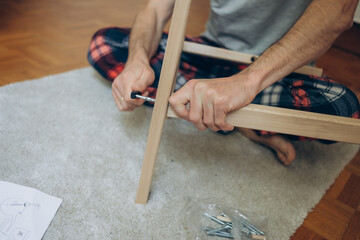  a man collects wooden furniture with his own hands while sitting on the floor in an apartment