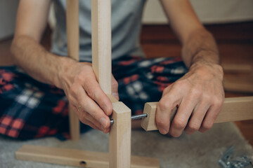  a man collects wooden furniture with his own hands while sitting on the floor in an apartment