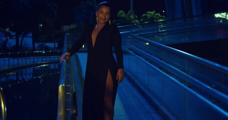 Sexy hispanic woman spins in the walkway of a glass building wearing a black dress at night