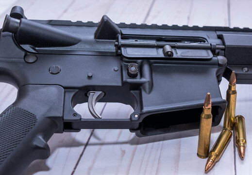 An AR15 rifle chambered in 223 caliber with four bullets next to it on a white wooden background