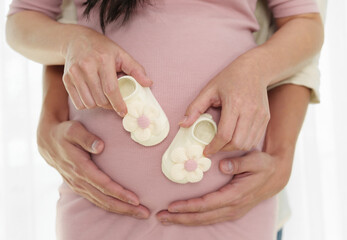 pregnant couple holding with hands together newborn baby shoes on belly