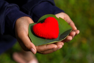 Young girl holding a heart on blur sky background. Valentine day, The child's hand gripped the red heart