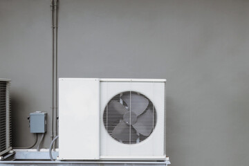 Outer air conditioner coil with hot draining fan, attached at gray concrete building wall