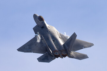 Very close top view of a F-22 Raptor in a  high G maneuver, with condensation trails forming  at the wing roots