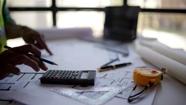 Close up of hands working and calculations estimate for cost and materials planning on paperworks and floor plan drawings about design architectural and engineering for houses and buildings.