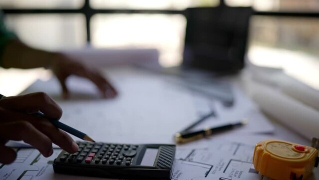 Close up of hands working and calculations estimate for cost and materials planning on paperworks and floor plan drawings about design architectural and engineering for houses and buildings.