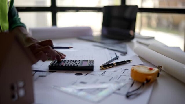 Close up of hands working and calculations estimate for cost and materials planning on paperworks and floor plan drawings about design architectural and engineering for houses and buildings.