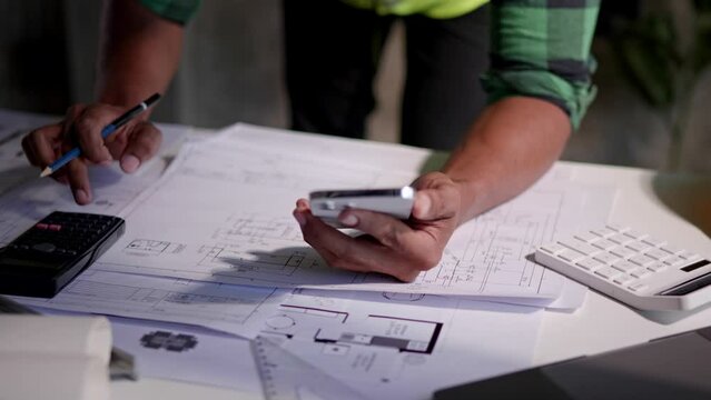 Close up of hands working and calculations estimate for cost and materials planning on paperworks and floor plan drawings about design architectural and engineering for houses and buildings.