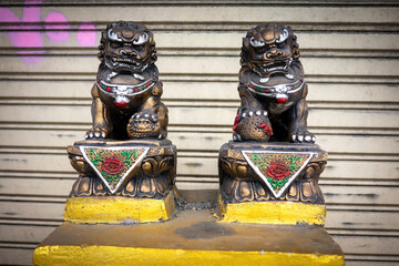 Two seated Chinese painted bronze dragon statues in front of a closed roller shutter.