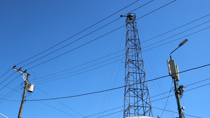Cords of power, transformers, lamps and electric poles on the clear blue sky background. Cables. Electricity supply in the downtown city.