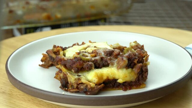 Springling parmesan cheese on a slice of delicious homemade italian food lasagna in rotation brown ceramic plate on wooden board.