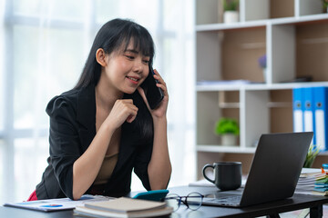 Business freelance asian woman talking on phone and working on laptop computer managing her business in workplace, doing business plan on calculator accounting financial report.