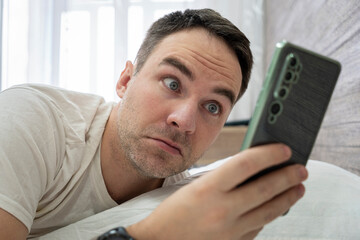 Wake up shocked guy late for work in morning. Man surprised to hear ringing of alarm smart phone,...