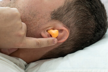 beautiful young man sleeping, in the ears orange earplugs against street noise, salvation from...