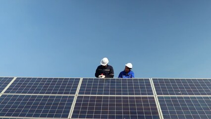 Male and female electrician technicians boarding forklift for maintenance checking solar cell panels that are shaky being fixed with team of technicians using electric drill to tighten for safety. - Powered by Adobe