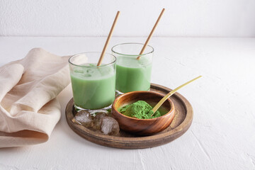 delicious healthy matcha latte tea in two glasses with straw and ice pieces on a round wooden tray. an alternative to coffee. invigorating drink.